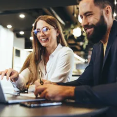 a man with a beard and a woman with long hair and glasses working together on a laptop used on a location landing page for Gold Coast Insurance Brokers